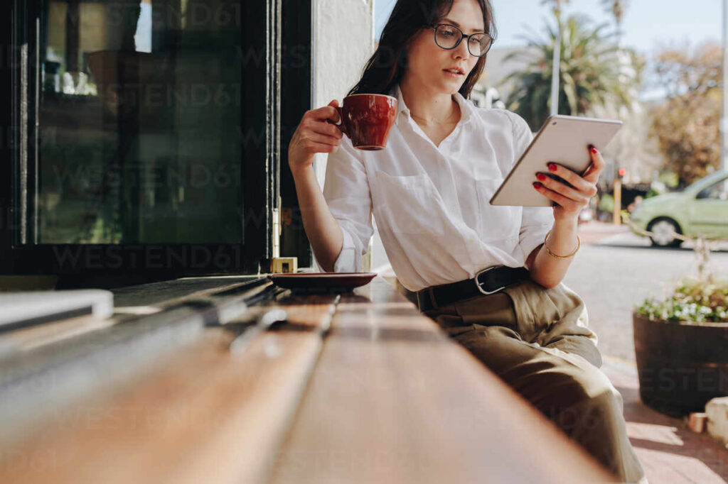 female entrepreneur relaxing at coffee shop having coffee and reading email on her digital tablet. businesswoman using digital tablet and drinking coffee at cafe.